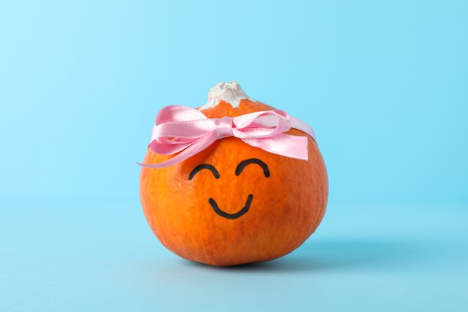 Happy pumpkin with bow on blue background, space for text