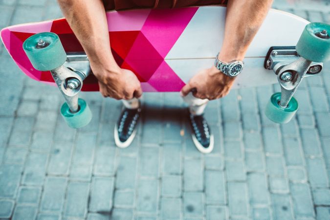 Sportive man carrying colorful longboard while standing on street