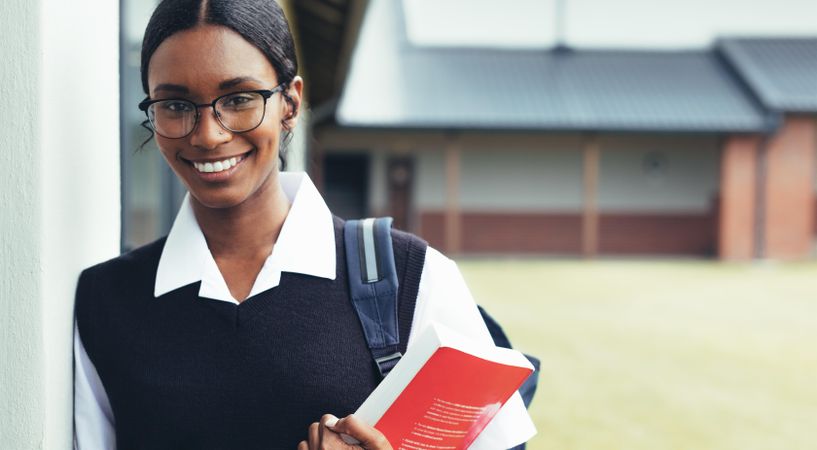 Teenage girl holding a textbook walking through the high school corridor