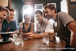 Group of friends sitting around a cafe table and looking at mobile phone 4dPGn4