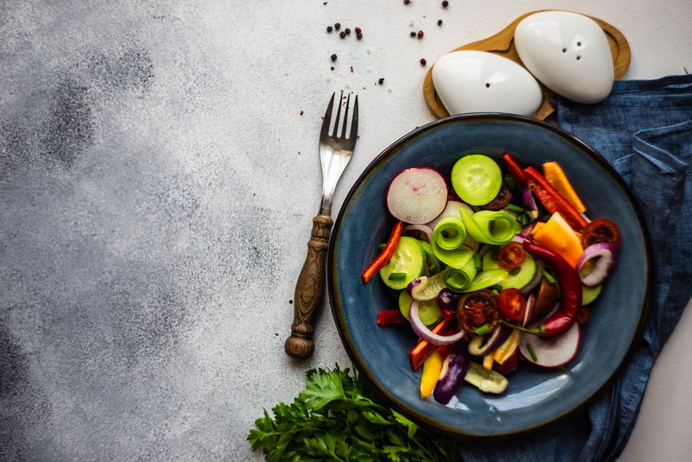 Top view of raw salad with chopped vegetables served with garnish on blue plate with copy space