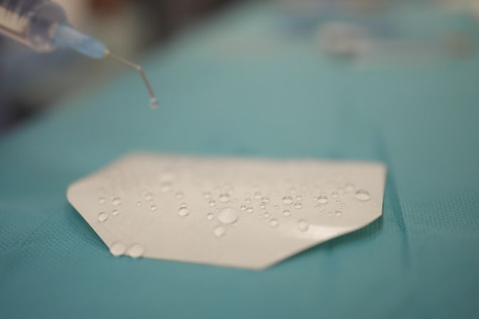 Drop of liquid on paper falling down from syringe