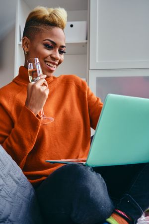 Black woman talking on a video call on her a laptop with champagne flute in a modern studio