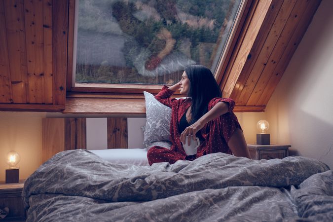 Woman on bed in cottage looking out of window