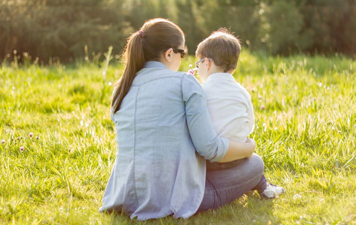 Cute son giving a bouquet of flowers to his mother sitting in a field