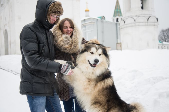 Brother and sister petting Siberian husky on snow covered ground