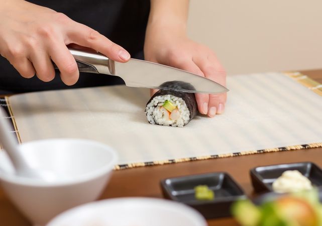 Female chef cutting Japanese sushi rolls with filling in nori seaweed sheet