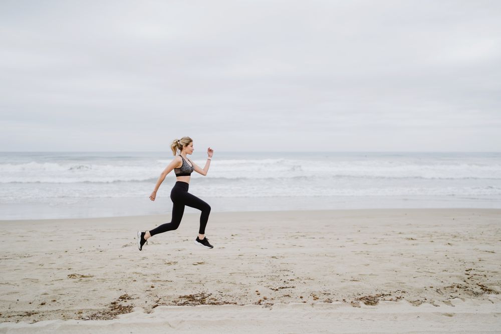 Young female athlete in active wear jogging while jumping at sea beach