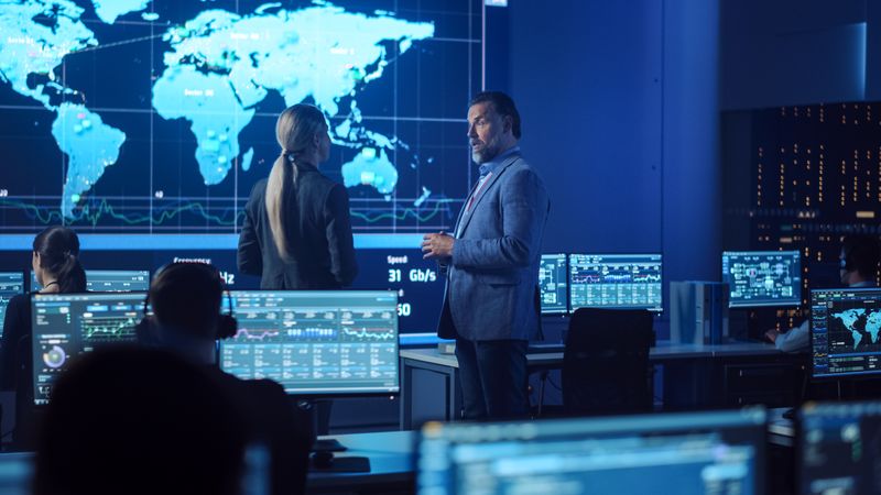 Executives Discuss Global Data in Futuristic Command Center. Analysts Monitor Screens Displaying Worldwide Information. Large World Map Projection Dominates, Showcasing International Operations and Real-time Data Flow.