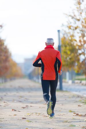 Back of male running on cement path in park in the fall