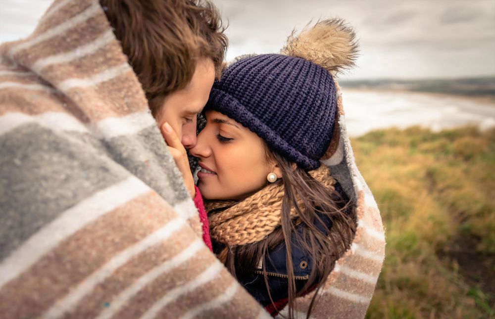 Close up of tender moment between a couple while wrapped in blanket on a windy day