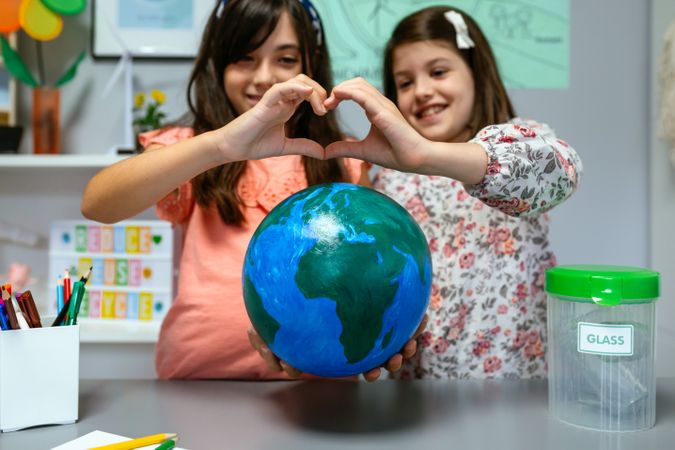 Two female students showing globe world earth while making heart shape with hands