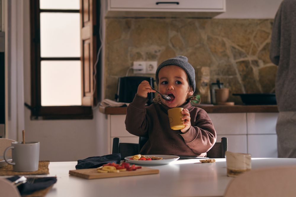 Cute boy eating from spoon and cup in kitchen