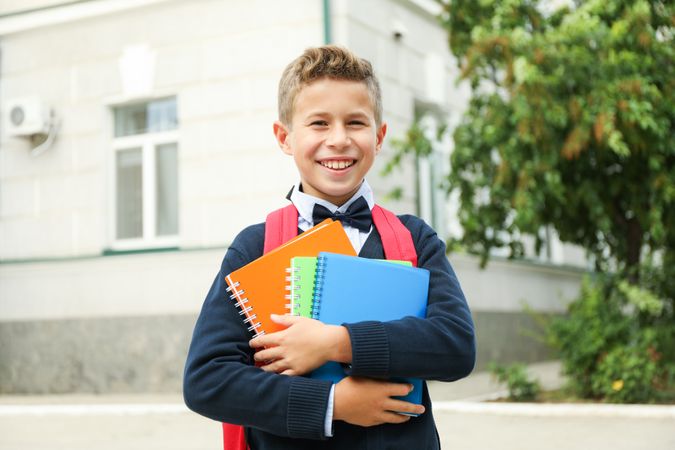 Boy with copybooks against school building, space for text
