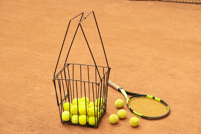 Racket and basket with balls on clay court