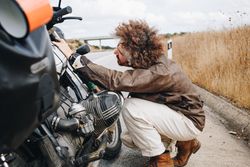 Man fixing motorcycle on hard shoulder of road