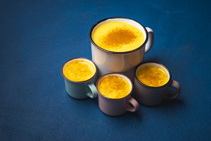 Cups of turmeric latte on blue table