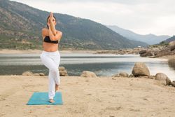 Woman practicing yoga outdoors near water
