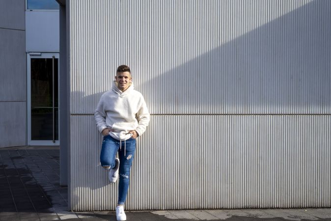 Portrait of young male with hands in pocket leaning on wall outside