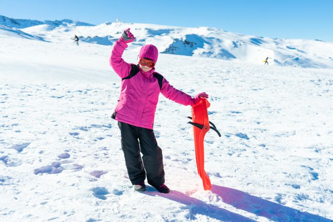 Child in pink snow suit standing on mountain with sled at resort