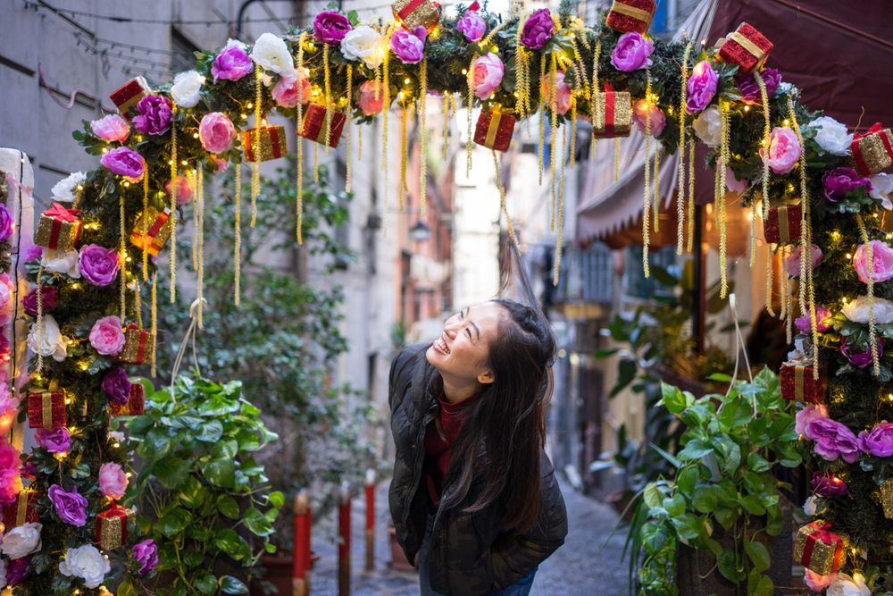 Satisfied Asian female traveler in casual wear walking on festive beautiful street