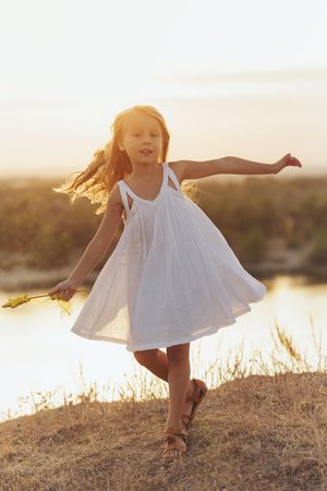 Blonde female child in summer dress playing in front of lake with star wand