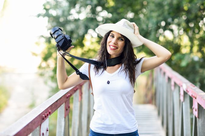 Woman walking with SLR camera, wearing straw hat outside