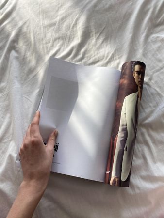 Arm leafing through a magazine on bedsheets