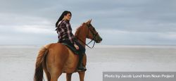 Woman horse riding at the sea shore and looking away 4Opngb