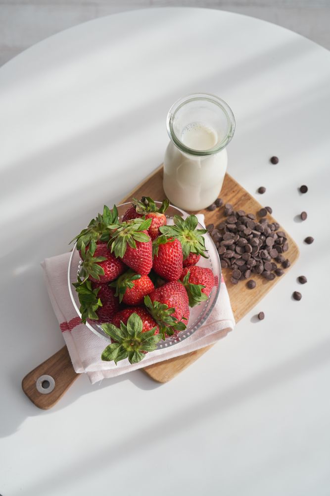 Delicious strawberries in bowl and milk in glass bottle on wooden