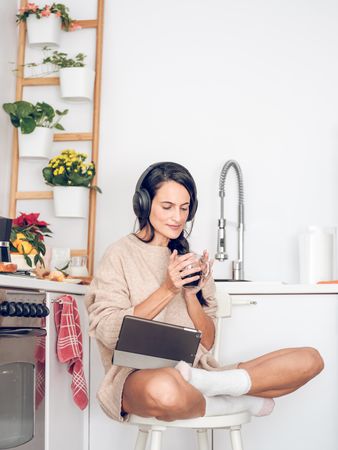 Woman in headphones with coffee and tablet sitting on chair