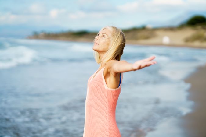 Carefree older woman standing on the coast with her arms outstretched
