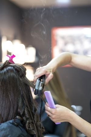 Long brunette hair being curled by stylist with ceramic hair iron