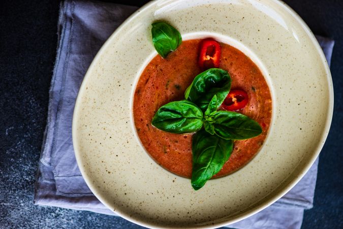 Elegant ceramic bowl of gazpacho soup with basil leaves and pepper garnish