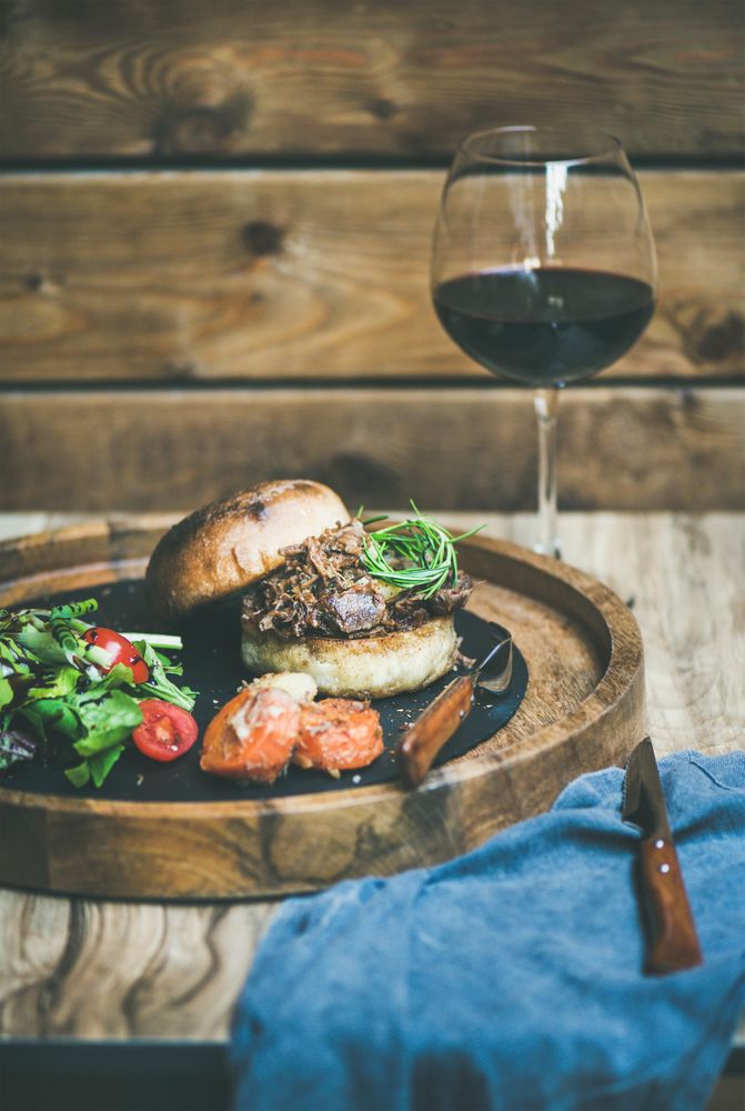 Pulled pork sandwich with red wine at wooden restaurant table