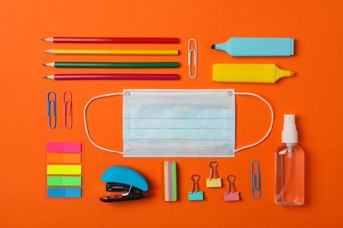 Flat lay with school supplies, medical mask and sanitizer on orange background