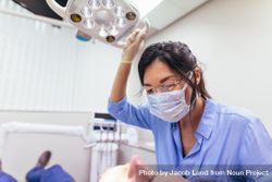 Female dentist wearing mask adjusting light with patient on chair at dental clinic 4BRVB4