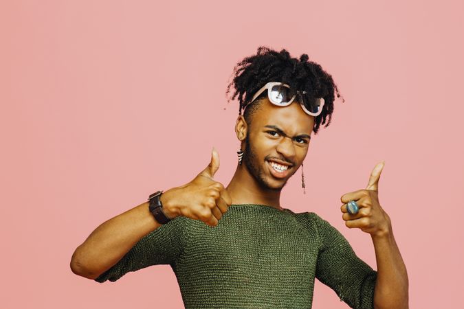 Portrait of a laughing man in green shirt pointing with thumbs up, with pink copy space around him
