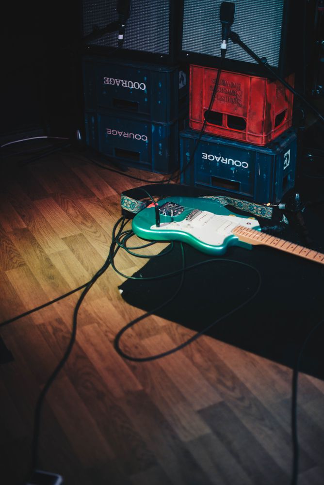 Teal electric guitar and amplifiers stacked on crates on stage at concert venue
