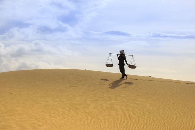 Rice farmer wearing conical hat and holding carrying pole in desert
