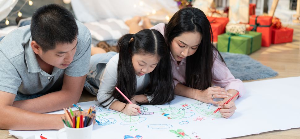 Happy Asian family drawing on paper together in the living room