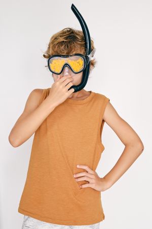 Boy in snorkeling goggles with petals covering nose on light bac