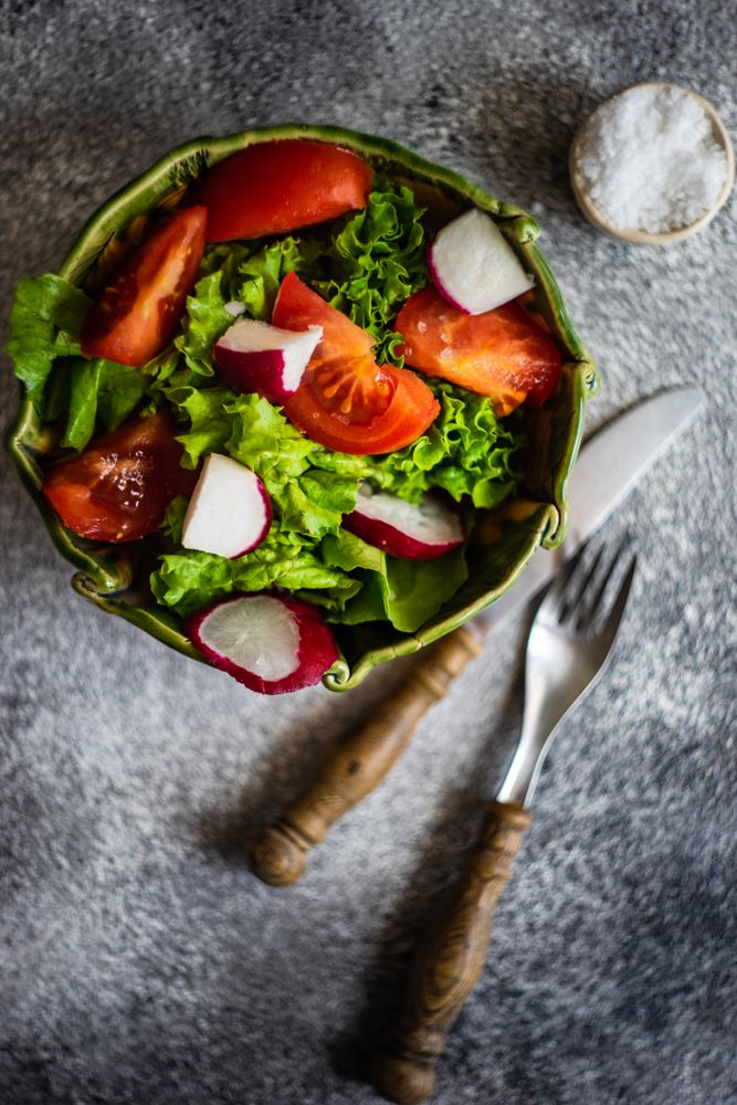 Top view of salad with tomatoes, radish & lettuce on concrete background with copy space