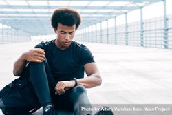 Black man sitting on bridge checking smart watch after training 4Av8qb