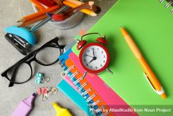 Pile of colorful notebooks with alarm clock, pencils and stationary bejeA0