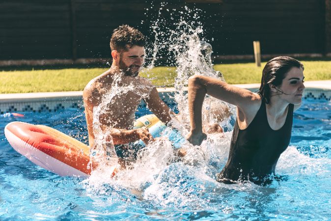Young woman splashing on man sitting on airbed in the pool