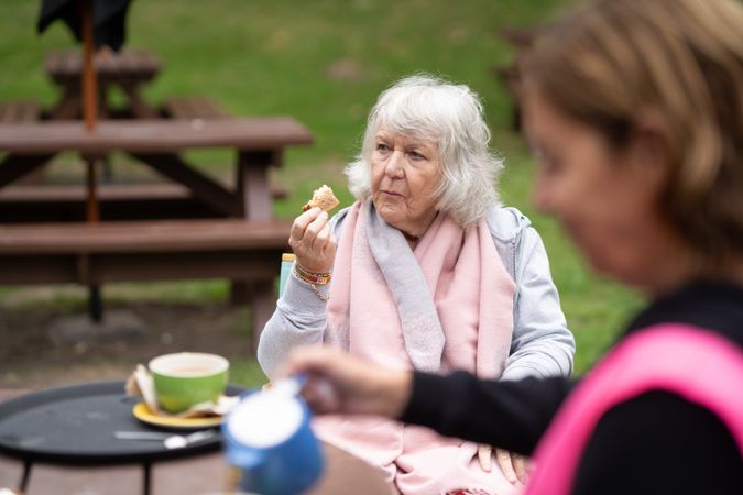 Older woman sitting outside at park bench enjoying tea break