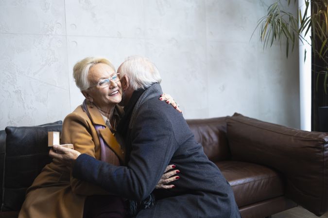 Older man holding engagement ring box and embracing woman after proposing