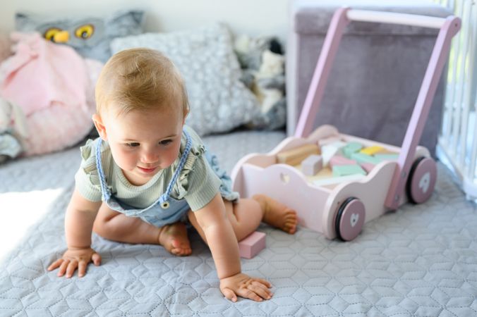 Happy baby near toy cart and blocks on bed