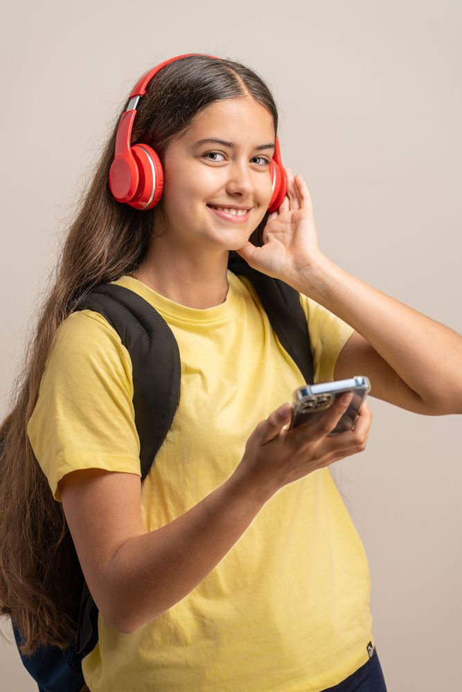A happy young student listening to music with red headphones and holding a smartphone.